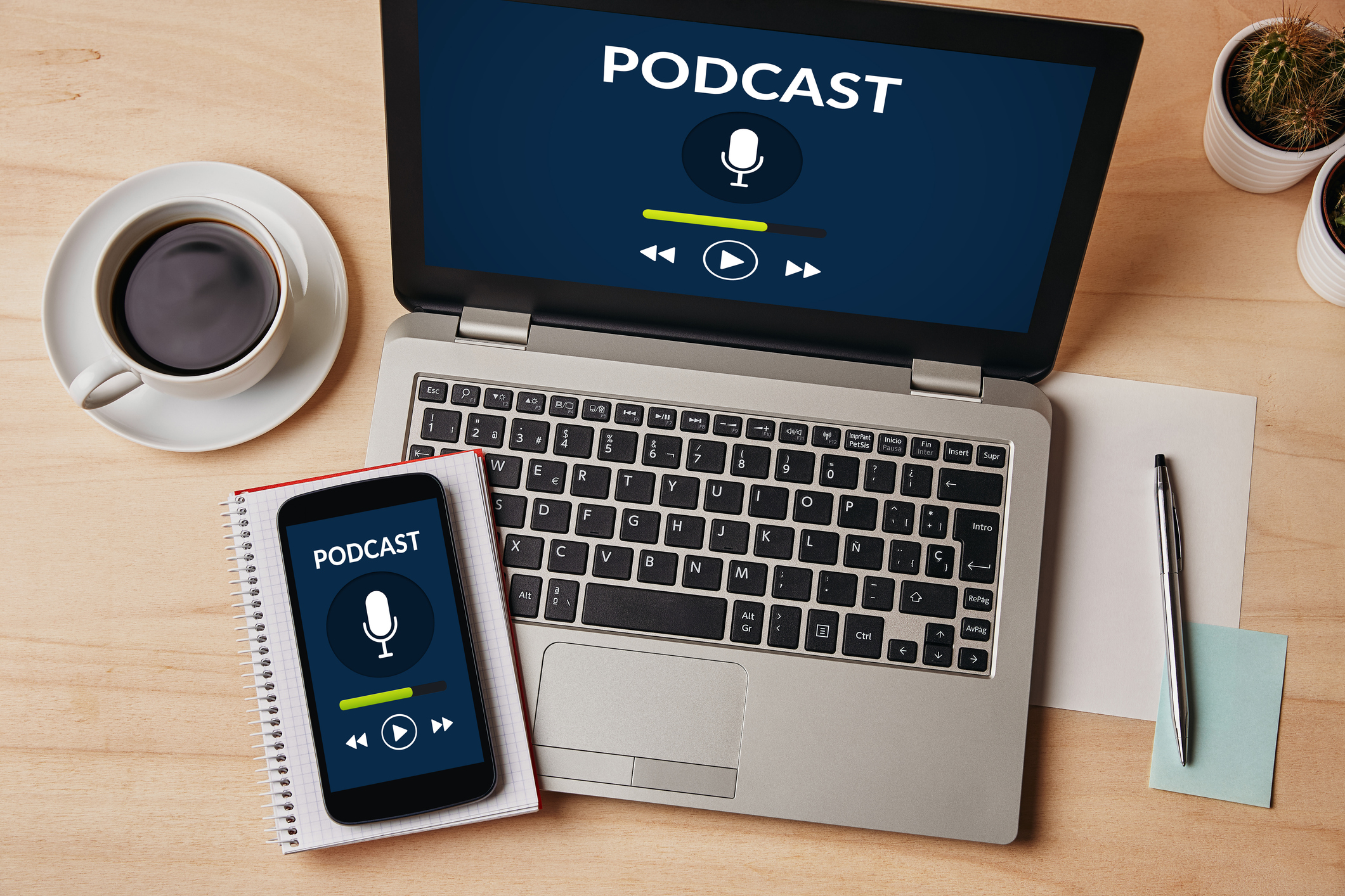 Podcast imagery is displayed on an open laptop and smartphone laying on a desk in a work environment.